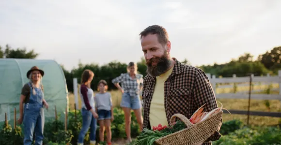 Personnes dans un champ cultivé dont l'homme en premier plan tient un panier en osier remplis de légumes.