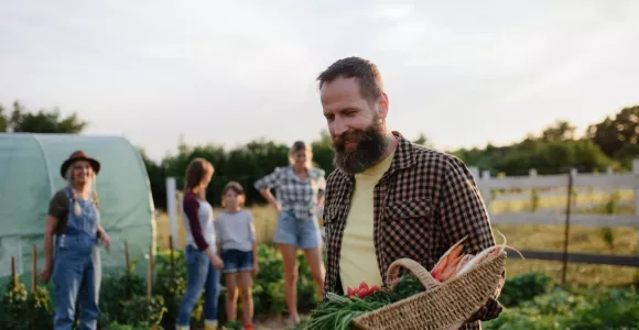 Personnes dans un champ cultivé dont l'homme en premier plan tient un panier en osier remplis de légumes.