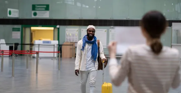 Homme voyageur arrivant avec une valise jaune vers une femme dans un hall d'aéroport.