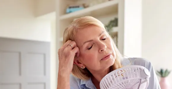 Femme blonde assise devant un bureau et tenant dans la main gauche un ventilateur à main.