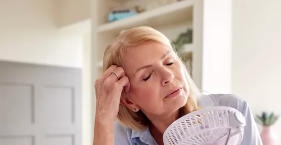 Femme blonde assise devant un bureau et tenant dans la main gauche un ventilateur à main.