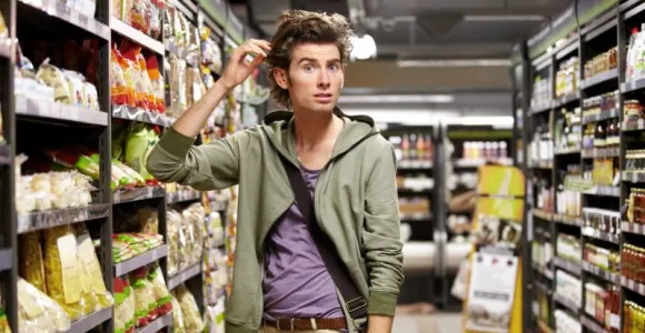 Jeune homme confus dans un rayon de pâtes d'un supermarché. 