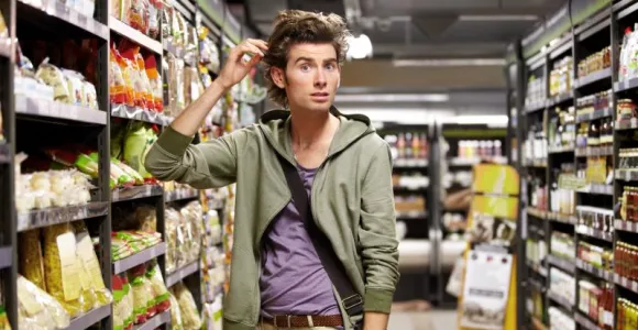 Jeune homme confus dans un rayon de pâtes d'un supermarché. 