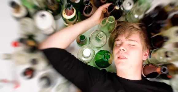 Un jeune couché entouré de bouteilles d'alcool vides