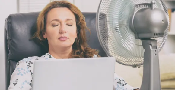 Femme assise sur un fauteuil un ventilateur lui souffle de l'air sur le visage