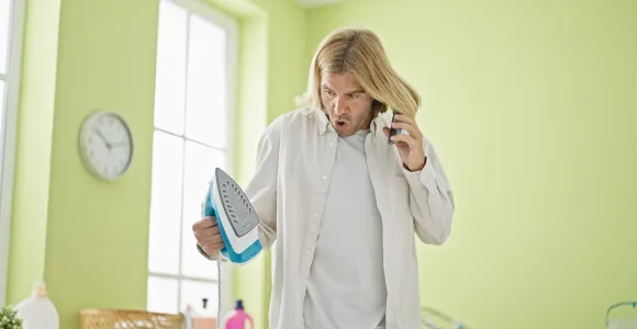 Homme paniqué avec un fer à repasser dans une main et un téléphone à l'oreille