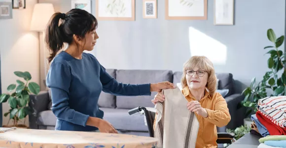Une aide ménagère sociale aide une dame en chaise roulante pour le repassage