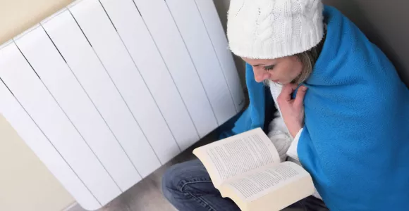 Une femme se réchauffe près d'un radiateur et lit un livre