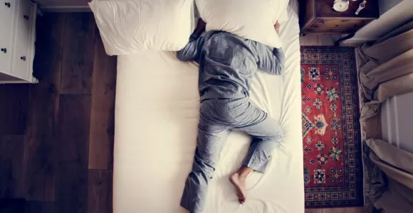 homme endormi sur un lit la tête sous un coussin 