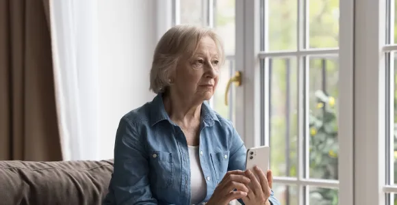 Une dame âgée assise sur un fauteuil tient un smartphone en main