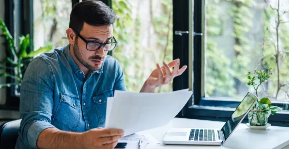 Un homme dubitatif en train de remplir sa déclaration fiscale devant son ordinateur