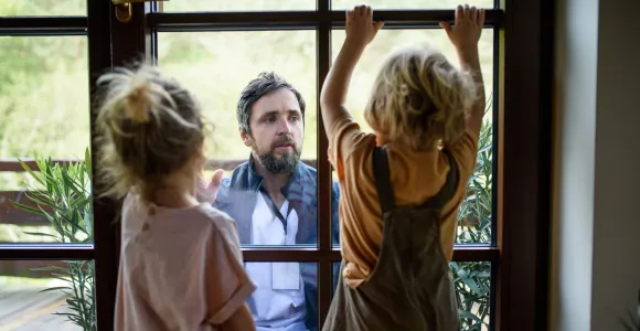 Un père communique avec ses deux enfants au travers d'une fenêtre fermée