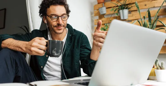 Un homme en télétravail boit un café derrière son ordinateur