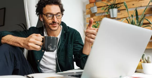 Un homme en télétravail boit un café derrière son ordinateur