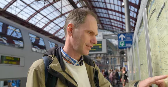Un homme sur le quaie d'une gare regarde les horaires des trains