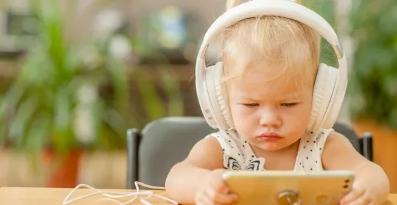 Un enfant en bas age porte un casque audio et regarde un écran de téléphone