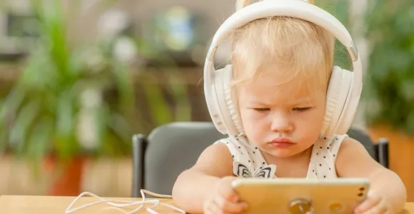 Un enfant en bas age porte un casque audio et regarde un écran de téléphone