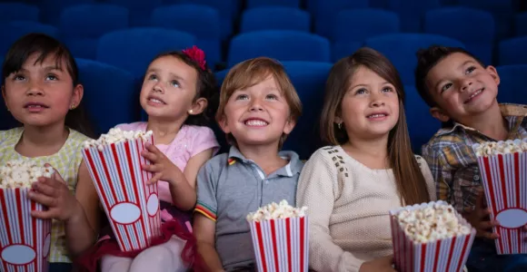 Cinq enfants assis dans une salle de cinéma avec des popcorns dans les mains