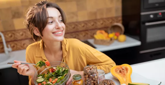 Femme sourit en mangeant une assiette de légumes crus