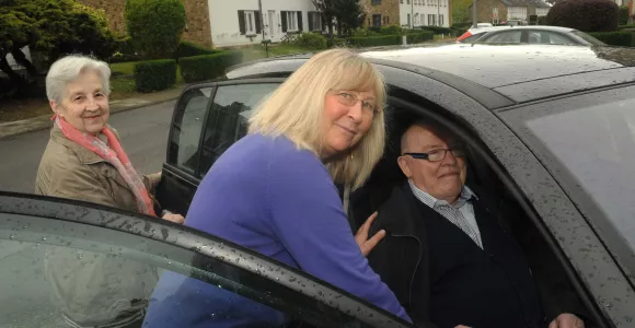 Des bénévoles d'Altéo aident un homme âgé à entrer dans une voiture