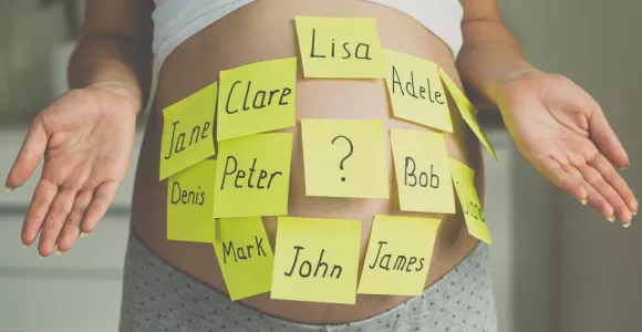 Photo d'un ventre de femme enceinte avec des post-it collés dessus sur lesquels sont écrits des prénoms