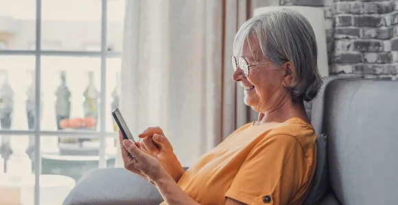 Une dame âgée assise dans un fauteuil consulte son smartphone