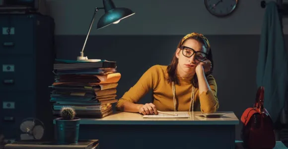 Femme dépitée assise sur un bureau entourée de piles de documents