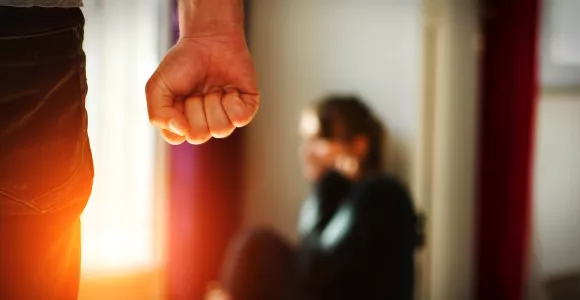 Un homme le poing serré se dirige vers une femme se protégeant au sol