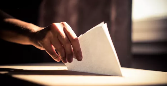 main déposant un bulletin de vote dans une urne