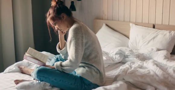 Ado lisant un livre assise sur son lit