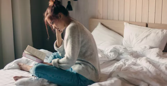 Ado lisant un livre assise sur son lit