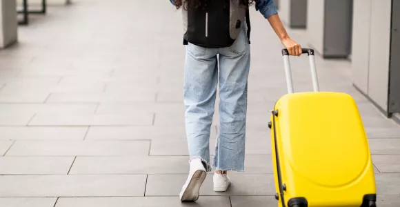 femme de dos tirant une valise jaune