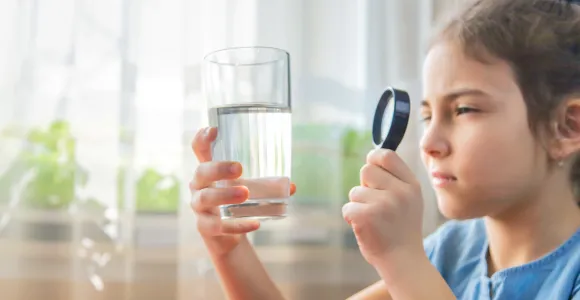 une petite fille inspecte un verre d'eau avec une loupe
