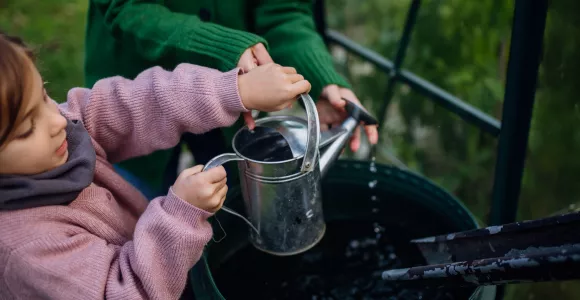 Une fillette et sa maman récupèrent de l'eau de pluie dans un arrosoir. 