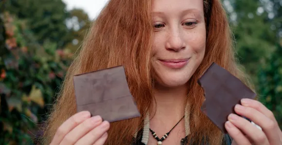 une jeune femme rousse regarde deux morceaux de chocolat