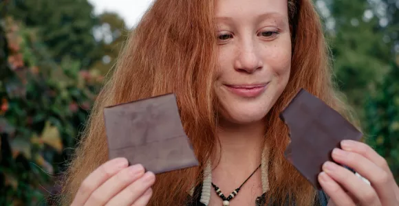 une jeune femme rousse regarde deux morceaux de chocolat