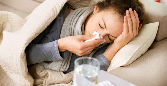 une femme malade se mouche le nez couchée sous une couverture
