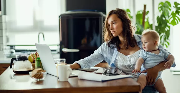 Une femme regarde un document, l'air fatigué et un bébé dans les bras.