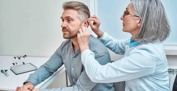 Une audicienne place un appareil auditif dans l'oreille d'un monsieur