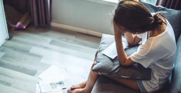 Une jeune femme se prend la tête dans les mains devant un amas de factures qui s'accumulent