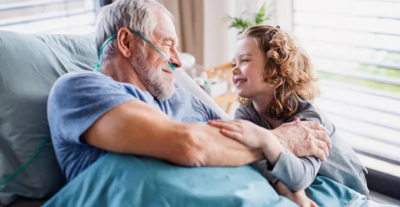 un monsieur alité sur un lit d’hôpital parle avec sa petite fille
