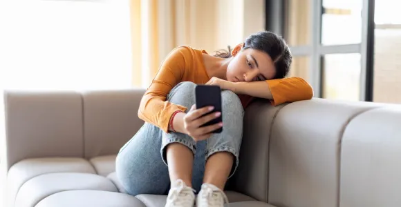 Une jeune fille dans un canapé regarde avec ennui son téléphone.