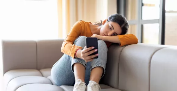Une jeune fille dans un canapé regarde avec ennui son téléphone.