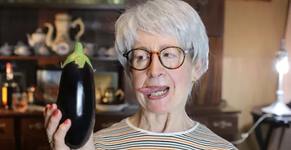 Une senior tient une aubergine en main en la regardant d'un air coquin.