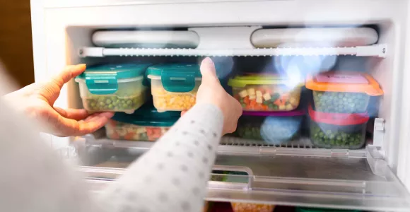 une dame prend des boites d'aliments au congélateur