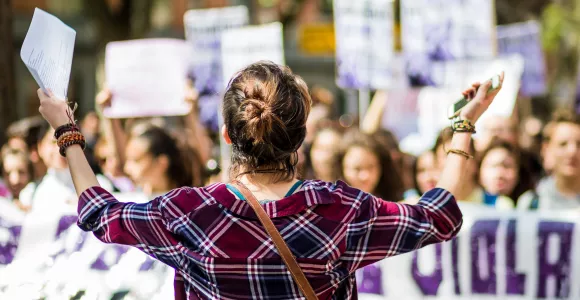Une jeune femme de dos ouvrent ses bras vers d'autres femmes en train de manifester pour les droits des femmes.