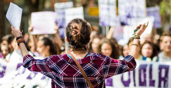 Une jeune femme de dos ouvrent ses bras vers d'autres femmes en train de manifester pour les droits des femmes.
