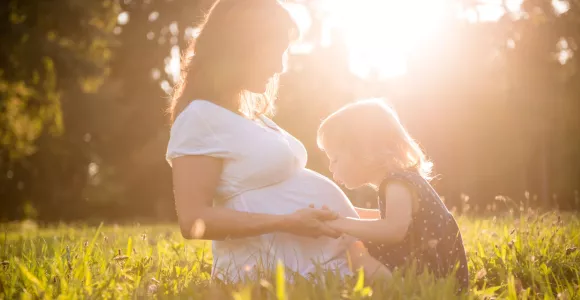 une petite fille embrasse le ventre de sa maman pour protéger la santé du bébé pendant les 1000 jours