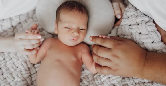 un bébé entouré des mains de ses parents