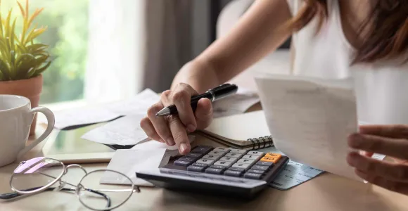 Une femme tape des montants de dépenses sur sa calculatrice